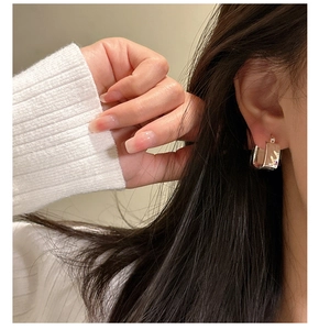 Close-up of silver square hoop earrings with pleated texture worn by a model