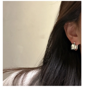 Detail of square textured S925 silver hoop earring worn on an ear with polished finish
