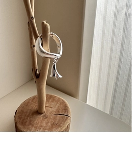 Detailed close-up of a silver bell ring hanging on a rustic wooden jewelry stand