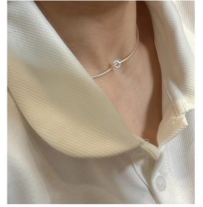 Detail of silver knot snake chain necklace worn with a white knitted polo shirt