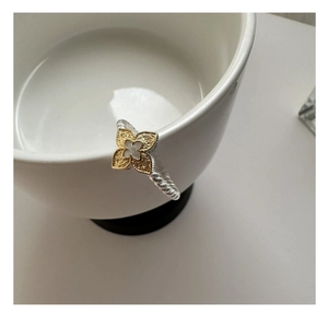 Macro detail of S925 silver rope band and gold floral clover ring on a white ceramic bowl