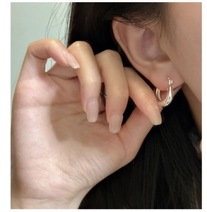 Macro shot of minimalist silver S925 U-shaped drop earrings worn on ear and hand