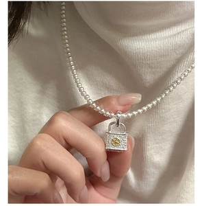 Close-up of S925 silver vintage lock pendant with gold flower on white pearl necklace