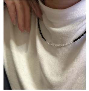 Detail of beaded necklace with black onyx and textured silver beads on white knit collar