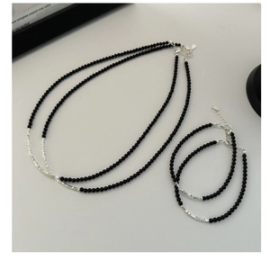 Detailed close-up of minimalist black bead jewelry with silver textured metal tubes