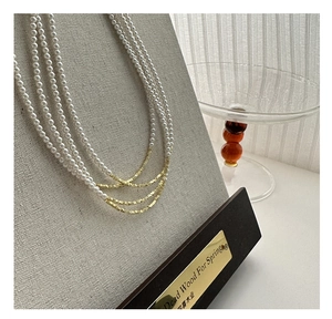 Dettaglio di una collana a tre strati di perle con perline dorate sfaccettate su supporto