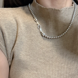 Collier à perles en argent 925 avec fermoir à crochet porté sur fond beige