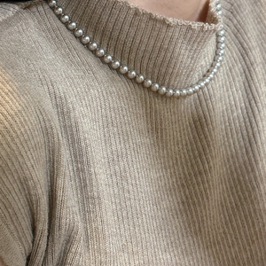 Gros plan d'un collier de perles argentées 925 porté sur un pull en maille kaki clair