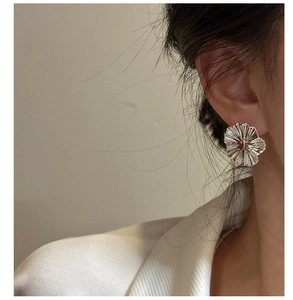 Macro detail of a large textured silver flower earring worn on a model's earlobe
