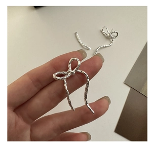 Close-up of silver bow earrings with hammered metal texture on minimalist background