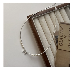 Detail of silver chain necklace with baroque pearls and a delicate metal bow pendant