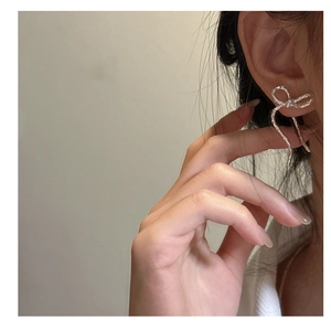 Detail of silver bow earrings with hammered metal texture worn on a female model