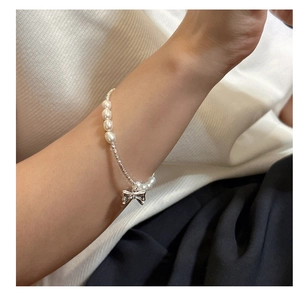 Detailed view of handmade S925 silver bow pendant and white pearls on woman's wrist