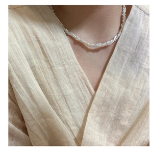 Detail of elegant S925 silver pearl necklace layered on beige fabric with twisted design