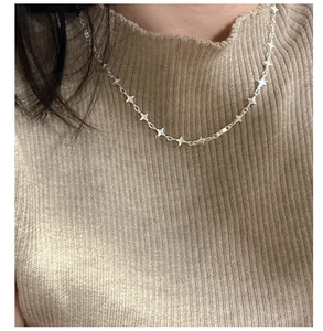 Detail of S925 silver four-pointed star necklace worn over a beige knit sweater