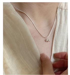 Detailed view of a silver cherry pendant necklace with sleek snake chain on a model