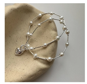 Detail of silver heart charm with star engraving on double-layer pearl bracelet