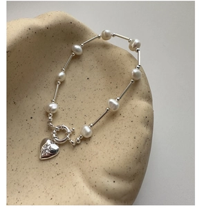 Close-up of S925 sterling silver pearl bracelet with star engraved heart charm on ceramic