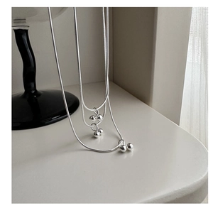Close-up of three sterling silver snake chain necklaces with double cherry ball pendants