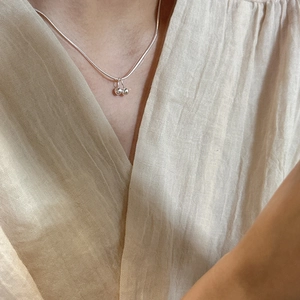 Minimalist 925 sterling silver cherry pendant necklace worn by a model on a beige fabric background