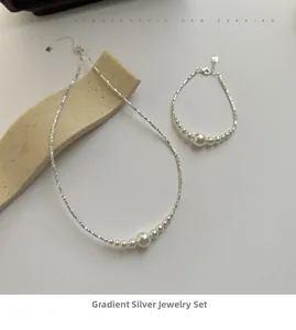 Detail of S925 silver necklace and bracelet set with gradient pearls on a grey background