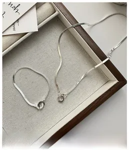 Detailed view of silver S925 double-ring snake chain necklace and bracelet on linen tray