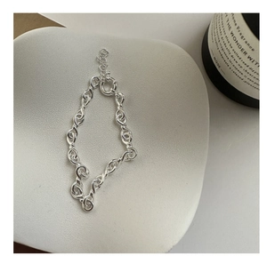 Close-up of twisted silver knots and link chain bracelet on ceramic tray decor