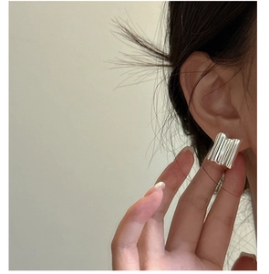 Close-up of wavy square silver hoop earrings with a modern fluid metal texture on ears