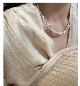 Close-up of layered silver bead necklace showing fine metallic luster on a model