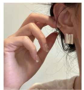 Close-up of square silver hoop earrings with vertical wavy texture worn on ear