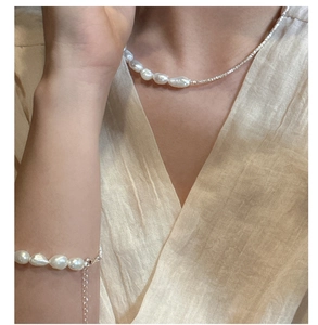 Detail of baroque pearl necklace and bracelet set on a beige linen shirt