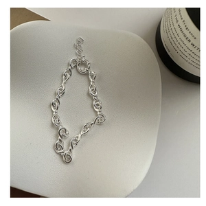 Macro detail of silver twisted link chain bracelet on a minimalist white display tray