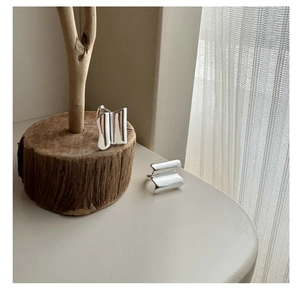 Close-up of wavy S925 sterling silver hoop earrings on a minimalist wooden base
