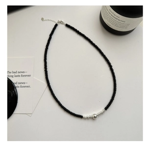 Detail of beaded necklace with black onyx beads and silver ball on a minimalist background