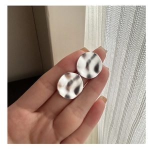 Nahaufnahme silberner Ohrstecker mit Hammerschlag-Textur und unregelmäßigem rundem Design