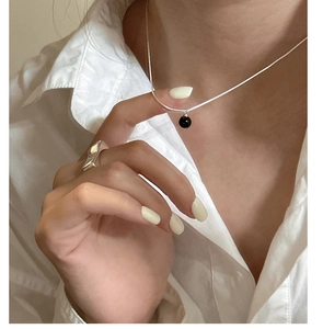 Detail of a minimalist silver wave ring and black agate ball pendant on a model