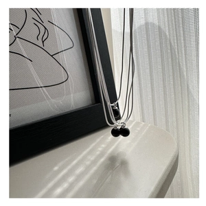 Detailed view of silver S925 snake chain with black agate ball pendant on wooden frame
