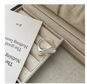 Gros plan sur une bague carrée en argent posée sur une boîte à bijoux en tissu beige