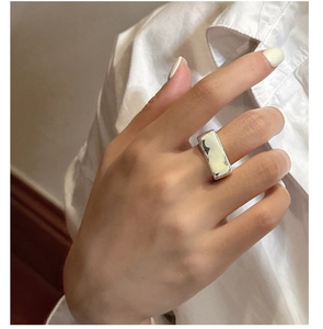 Gros plan sur une bague carrée minimaliste en argent portée à l'index avec fini brillant