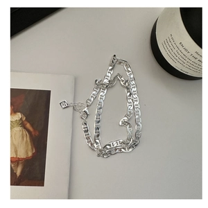 Dettaglio della collana in argento S925 con maglie a H e logo tag su fondo grigio