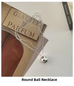 Vue macro d'un pendentif boule en argent minimaliste sur une fine chaîne à billes