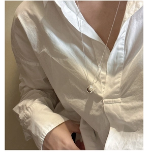 Détail d'un collier avec pendentif boule argentée porté sur une chemise blanche