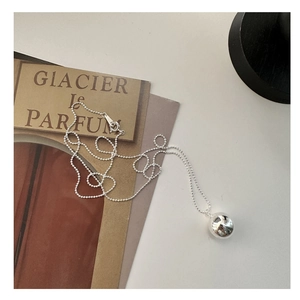 Détail d'un pendentif boule en argent minimaliste sur une fine chaîne de billes