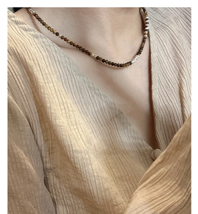 Détail du collier en argent 925 avec œil de tigre porté sur un vêtement en soie