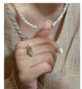 Detail of S925 silver irregular pearl necklace and geometric ring on a soft fabric