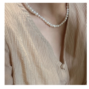 Detailed close-up of natural irregular freshwater pearl strand on neck with linen shirt