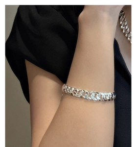 Gros plan d'un bracelet gourmette en argent sur un poignet avec une manche noire
