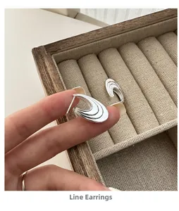 Detail of S925 sterling silver curved line stud earrings held against a wooden box