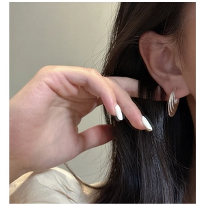 Close-up of a model wearing layered curved silver earrings with a modern geometric design