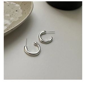 Close-up of polished S925 sterling silver C-shaped geometric hoop earrings on flat surface
